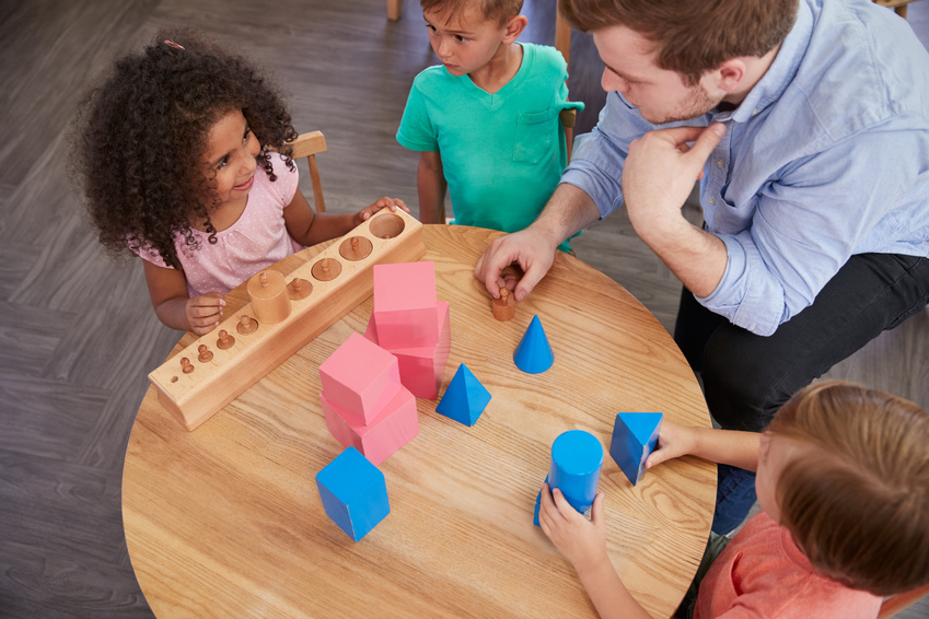 children and teacher sitting around table with 3D shapes
