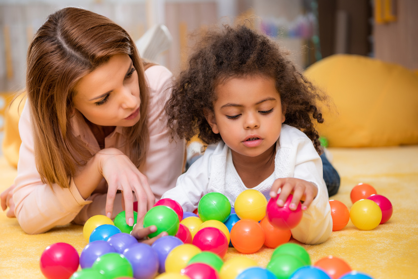 teacher and preschool child with colorful balls